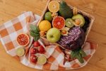 A colorful mix of fruits and vegetables arranged in a basket on a rustic wooden table.