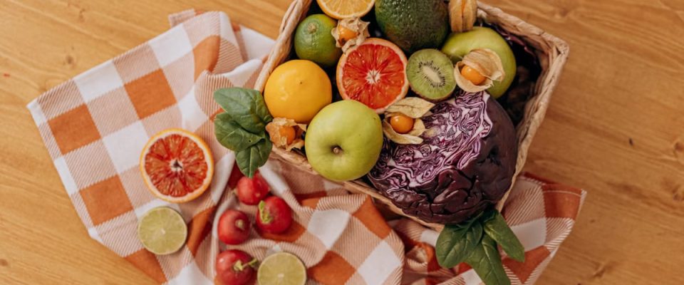 A colorful mix of fruits and vegetables arranged in a basket on a rustic wooden table.
